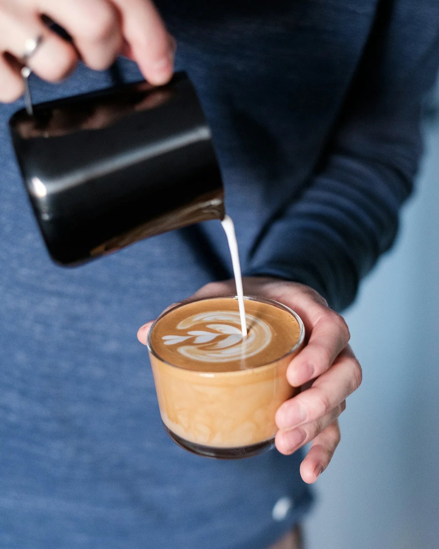 Barista vertiendo leche sobre un café con dibujo